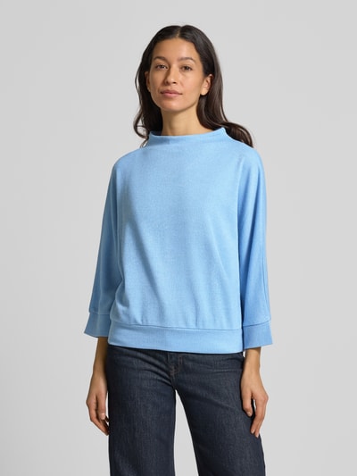 Frauenmodel trägt Longsleeve mit 3/4-Ärmel Modell 'Sagida' von Opus, hellblauer Material-Mix mit Viskose-Anteil, lockerer Schnitt, Stehkragen, gerippte Abschlüsse, Rückenlänge bei Größe 36: 60 cm, Ganzkörperansicht von vorne.