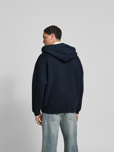 Männermodel trägt Oversized Sweatjacke aus Baumwoll-Mix von Dsquared2 in Dunkelblau, Kapuze mit Tunnelzug, Ganzkörperansicht Rückansicht.