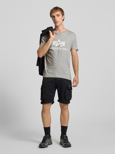 Männermodel trägt T-Shirt mit Logo und Rundhalsausschnitt von Alpha Industries in Grau, Reine Baumwolle, Regular-Fit, Ganzkörperansicht von vorne.