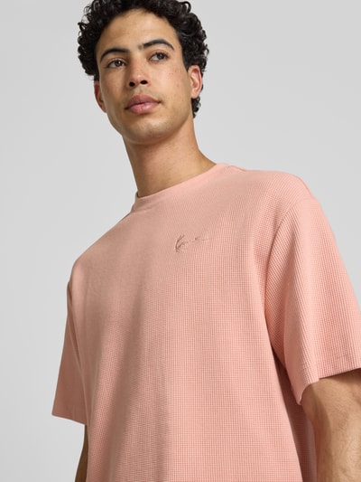 Männermodel trägt Oversized Fit T-Shirt mit Strukturmuster von KARL KANI in Rosa, Baumwoll-Mix, Logo-Stitching, Nahaufnahme Oberkörper.