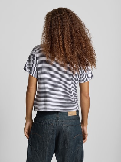 Frauenmodel trägt Relaxed Fit T-Shirt aus reiner Baumwolle mit geknotetem Saum von G-Star RAW, fein gestreift in Weiß und Dunkelblau, kombiniert mit dunkler Jeans, Ganzkörperansicht Rückansicht.