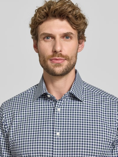 Männermodel draagt Regular Fit Businesshemd aus elastischem Baumwoll-Mix von Christian Berg Men met Kentkraag en Knoopsluiting, mix van katoen en elastaan, regular fit, maat 39/40: ruglengte 78 cm, schouderbreedte 48 cm, mouwlengte 66 cm, geruite stof in blauw en wit, Nahaufnahme Oberkörper.