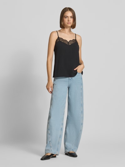 Frauenmodel trägt schwarzes Loose Fit Blusentop mit Spitzenbesatz Modell 'TIFFANY' von PIECES, kombiniert mit blauer Jeans, Ganzkörperansicht von vorne.