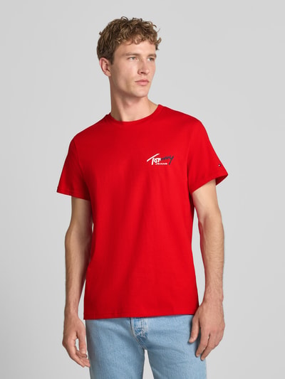 Männermodel trägt Slim Fit T-Shirt aus reiner Baumwolle von Tommy Jeans in leuchtendem Rot, glatte Struktur, Ganzkörperansicht von vorne.