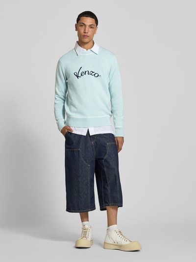 Männermodel trägt Leinenpullover aus Leinen-Mix von Kenzo in Hellblau mit Label-Stitching, Kontraststreifen, lockerer Passform, Ganzkörperansicht von vorne.