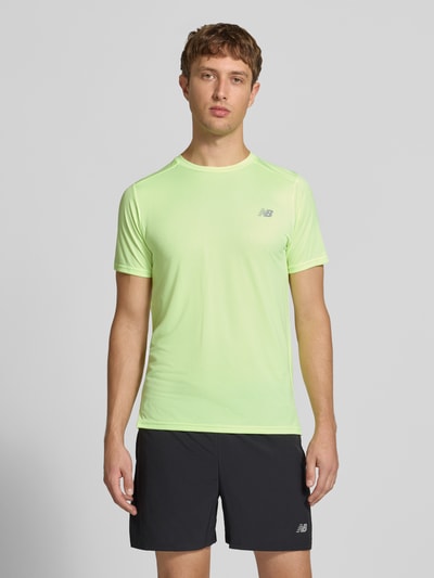 Männermodel trägt Funktionsshirt mit Rundhalsausschnitt und Logo von New Balance in Hellgelb, kombiniert mit schwarzen Shorts, Ganzkörperansicht von vorne. Rückenlänge bei Größe M: 69 cm, Regular Fit.