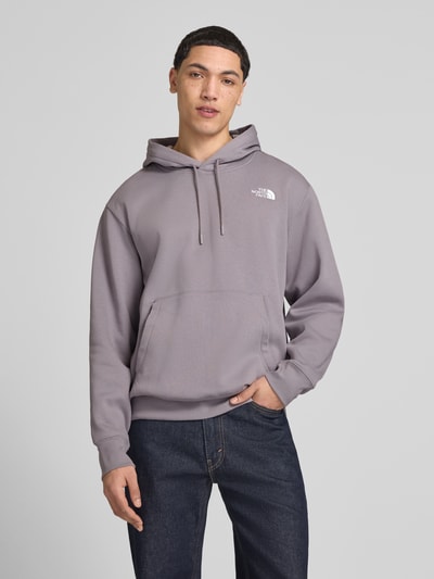 Männermodel trägt Regular Fit Hoodie mit Logo-Print von The North Face aus Baumwoll-Mix in Grau, Känguru-Tasche und Kapuze, Ganzkörperansicht von vorne. Rückenlänge bei Größe M: 70 cm, Ärmellänge: 73 cm.