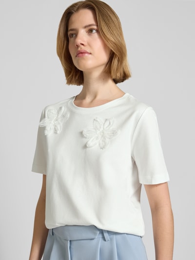 Frauenmodel trägt Regular Fit T-Shirt mit floralem Zierbesatz von monari aus Baumwoll-Modal-Mix, Rundhalsausschnitt, Nahaufnahme Oberkörper.