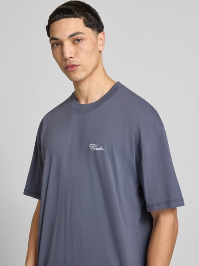 Męski model nosi Oversized Fit T-Shirt mit Logo-Stitching od Pegador z bawełny, krój oversized fit, wyhaftowane logo, okrągły dekolt, długość tyłu w rozmiarze M: 71 cm, zbliżenie na górną część ciała.