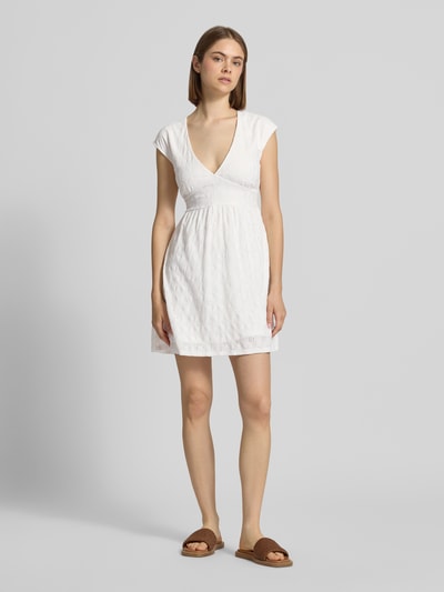 Frauenmodel trägt Kurzes Kleid mit V-Ausschnitt, Lochstickerei und großer Schleife von REVIEW, weiß, A-Linie, Material-Mix mit Stretch-Anteil, Ganzkörperansicht von vorne.