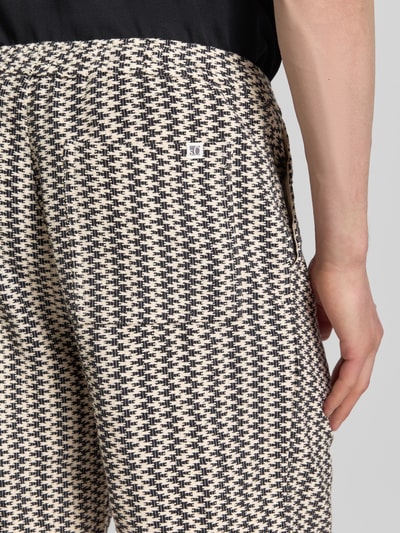 Männermodel trägt Relaxed Fit Stoffshorts aus Baumwoll-Mix von s.Oliver RED LABEL mit Optik: Allover-Muster, Strukturmuster, Label-Patch, seitliche Eingrifftaschen und Gesäßtasche aus reine Baumwolle, Nahaufnahme Gesäßtasche.