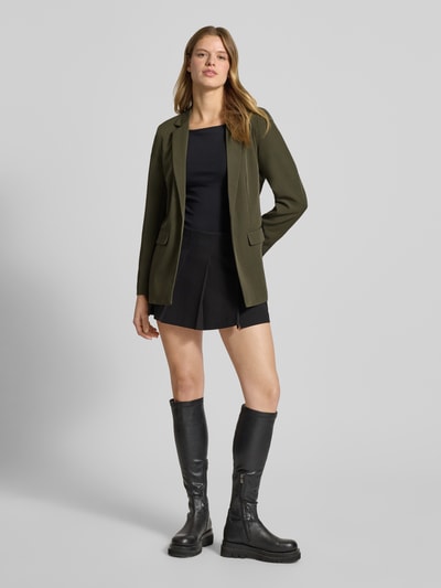 Kobiece modelka nosi Loose Fit Longblazer mit Abnähern Model 'BOZZY' od Pieces, efekt: jednolity kolor, krój loose fit, kołnierz z połami, długi rękaw, kieszenie z patką, wyhaftowane logo, bez zapięcia, całkowity widok z przodu.