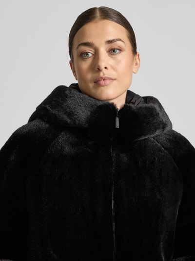 Frauenmodel trägt Kunstfelljacke mit Kapuze von Emporio Armani in Schwarz, glatte Struktur, Raglanärmel, Nahaufnahme Oberkörper.