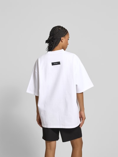 Vrouwenmodel draagt Oversized T-Shirt mit Label-Patch van black palms, wit katoen, ronde hals, halflange mouwen, ruglengte 73 cm, Ganzkörperansicht Rückansicht.