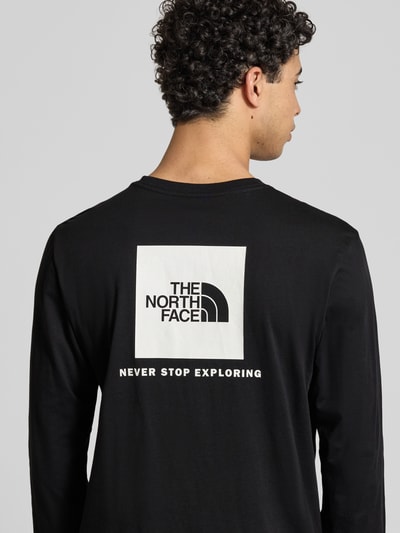 Męski model ma na sobie Regular Fit Longsleeve mit Logo-Print od The North Face, czarny bawełniany krój regular fit, długi rękaw, logo z tyłu, okrągły dekolt, elastyczne mankiety, długość tyłu w rozmiarze M: 69 cm, zdjęcie tyłu od góry do pasa