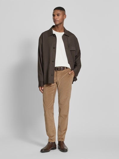 Männermodel trägt Slim Fit Cordhose mit Gesäßtaschen Modell 'Fabio' von Brax in Beige, feine Rippenstruktur, Ganzkörperansicht von vorne. Elastischer Baumwoll-Mix, schmale Passform, Eingrifftaschen, Knopf- und Reißverschluss.