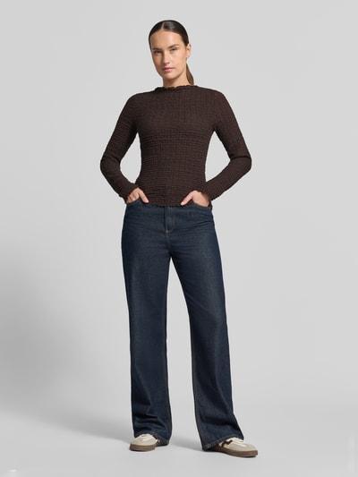 Frauenmodel trägt Regular Fit Langarmshirt aus Baumwoll-Mix Modell 'ZIA' von VERO MODA in Dunkelbraun, strukturierte Oberfläche, dazu blaue Jeans; Ganzkörperansicht von vorne. Damen Langarmshirt von VERO MODA.