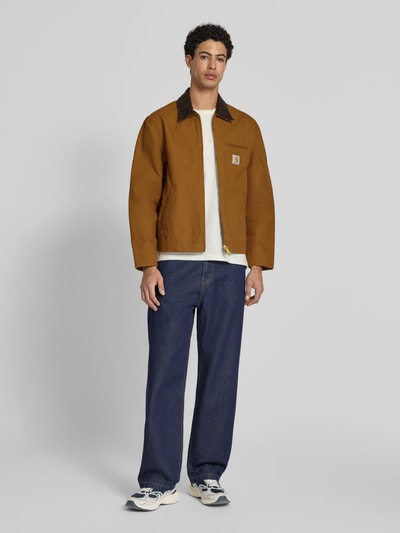 Männermodel trägt Jacke mit Label-Detail Modell 'Detroit' von Carhartt Work In Progress aus Reine Baumwolle, Regular-Fit, Ganzkörperansicht von vorne, warmes Braun, Umlegekragen, Reißverschluss, sichtbare Label-Detail, strukturierte glatte Oberfläche, Maßangaben Größe M: Rückenlänge 65 cm, Schulterbreite 47 cm, Brustweite 56 cm, Ärmellänge 64 cm.
