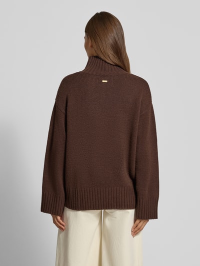Frauenmodel trägt Loose Fit Pullover aus Woll-Kaschmir-Mix von Barbour in Dunkelbraun, grobe Stricktextur, Ganzkörperansicht Rückansicht. Damen Pullover von Barbour.