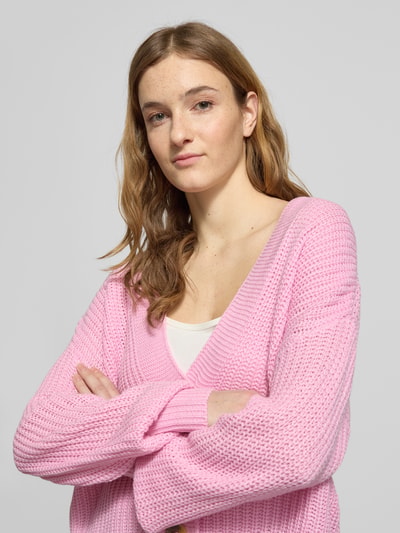 Frauenmodel trägt Regular Fit Strickjacke mit einreihiger Knopfleiste Modell 'CAROL NICE' von Only in Rosa, Strickoptik, Nahaufnahme Oberkörper.