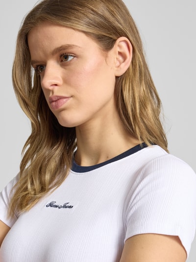 Frauenmodel trägt T-Shirt mit Rundhalsausschnitt und Label-Stitching von Guess Jeans, Baumwoll-Mix mit Modal-Anteil, Cropped, Nahaufnahme Oberkörper.