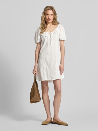 Frauenmodel trägt A-Linien Umstandskleid aus reiner Baumwolle Modell 'JUTTY' von Vero Moda, Optik: Unifarben, Struktur, Mini-Länge, Karree-Ausschnitt mit Binde-Detail, Ballonärmel, gerade, Elastisch, Ganzkörperansicht von vorne.