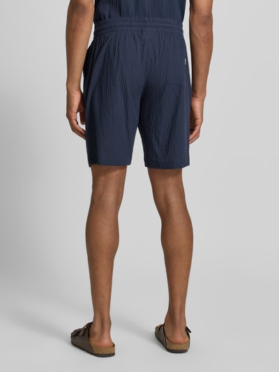 Männermodel trägt Shorts mit elastischem Bund und Strukturmuster von Lindbergh, Baumwoll-Mix mit Stretch-Anteil, Loose-Fit, Ganzkörperansicht Rückansicht.