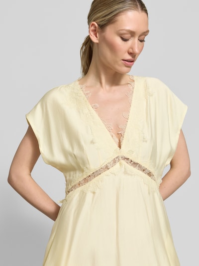 Frauenmodel trägt Midikleid mit V-Ausschnitt und Spitze Modell 'MOLLY' von Copenhagen Muse im Lyocell-Mix, Taillierter Schnitt, Kappärmel, Farbe hellgelb, fließende Textur, Ganzkörperansicht von vorne. Rückenlänge bei Größe S: 139 cm, Brustweite bei Größe S: 35 cm.