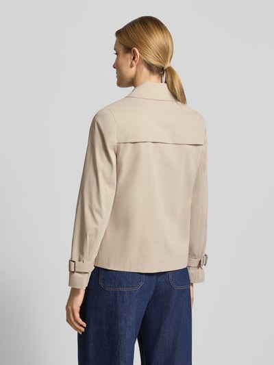 Modelka kobieca nosi trencz z zapięciem na guzik od MICHAEL Michael Kors, krój regular fit, wykładany kołnierz, dwurzędowy, beżowy, długość tyłu w rozmiarze S: 61 cm, szerokość ramion w rozmiarze S: 40 cm, szerokość klatki piersiowej w rozmiarze S: 52 cm, długość rękawów w rozmiarze S: 63 cm, gładka faktura, widok całej sylwetki od tyłu.