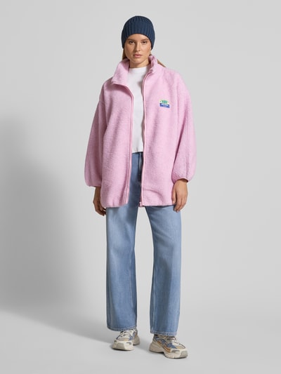 Vrouwenmodel draagt oversized jas met opstaande kraag, teddyfleece, rits, labeldetail, steekzakken, model 'HOKTOWN' van American Vintage, lichtroze, vooraanzicht hele lichaam.