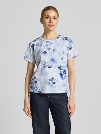 Frauenmodel trägt T-Shirt im Allover-Look mit Rundhalsausschnitt von monari, Baumwoll-Mix mit Modal-Anteil, Regular-Fit, Rückenlänge 53 cm, Größe 36, sanfte Blautöne mit floralen Mustern, glatte Textur, Ganzkörperansicht von vorne.