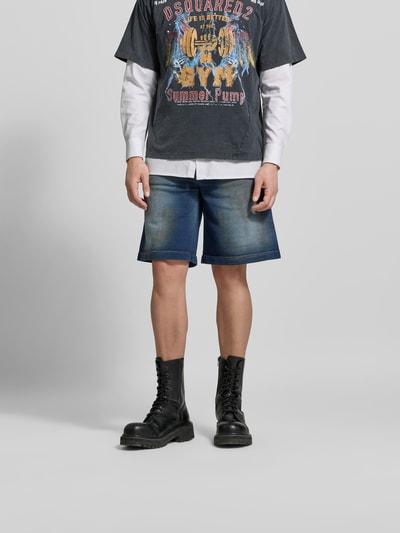 Männermodel trägt Baggy Fit Jeansshorts aus Baumwolle von Dsquared2 in Blau mit Eingriff- und Gesäßtaschen, Label-Detail, Ganzkörperansicht von vorne.