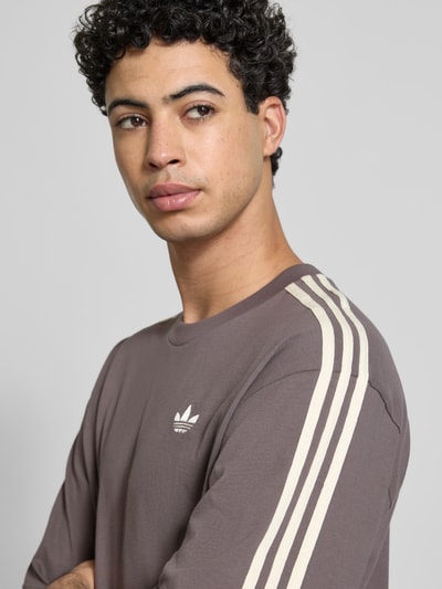 Männermodel trägt T-Shirt mit Label-Stitching von adidas Originals in bruin, losse fit, ribgebreide ronde hals, zuiver katoen, Nahaufnahme Oberkörper