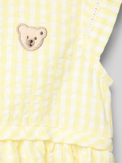 Mädchen trägt Regular Fit Kleid mit Logo-Detail von Steiff aus Reine Baumwolle, gelb-weiß kariert, Rüschenbesatz, Ärmelloses-Design, Detailaufnahme.