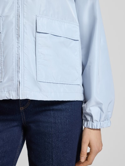 Kobieta nosi kurtkę Jacke mit Pattentaschen Modell 'CICAMI' od CINQUE w kolorze jasnoniebieskim, zamek błyskawiczny, kieszenie z patką, krój regular fit, wykładany kołnierz, detalicznie widoczne tekstury tkaniny, szerokość ramion w rozmiarze 36: 50 cm, szerokość klatki piersiowej w rozmiarze 36: 56 cm, długość tyłu w rozmiarze 36: 58 cm, długość rękawów w rozmiarze 36: 59 cm, detaliczne ujęcie przodu i rękawa – zbliżenie na dolną część.