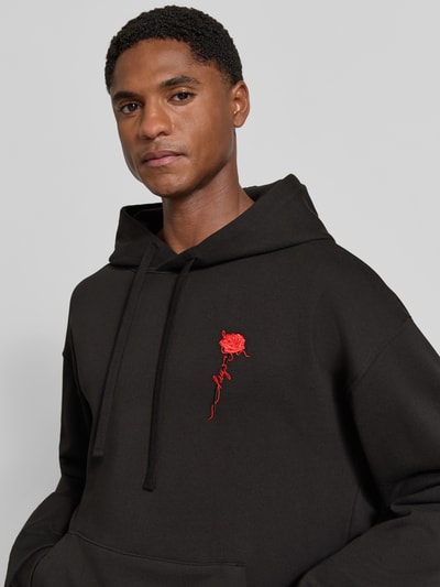 Männermodel trägt Regular Fit Hoodie aus reiner Baumwolle Modell 'Diflowhood' von HUGO in Schwarz mit rotem Logo, Nahaufnahme Oberkörper. Herren Hoodie von HUGO
