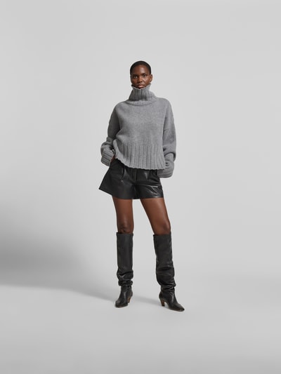 Frauenmodel trägt Shorts mit Leder-Anteil von Anine Bing im Material-Mix, ausgestellte Passform, Eingrifftaschen, Ganzkörperansicht von vorne.