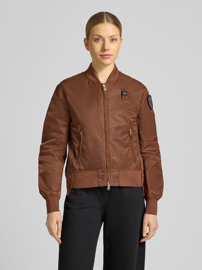 Frauenmodel trägt braune Bomberjacke mit Zweiwege-Reißverschluss, Label-Patches, seitlichen Reißverschlusstaschen von Blauer Usa, Ganzkörperansicht von vorne. Damen Modell 'LAURIE', Loose-Fit, Stehkragen, gerippte Abschlüsse, Rückenlänge 57 cm, Schulterbreite 44 cm, Brustweite 43 cm, Ärmellänge 62 cm.