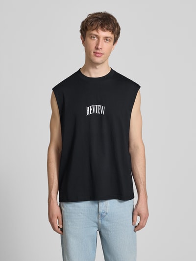 Männermodel trägt Muskelshirt mit Logo und Rundhalsausschnitt von REVIEW in Schwarz, Reine Baumwolle, Regular-Fit, Logo, Rückenlänge 68 cm, Ganzkörperansicht von vorne.