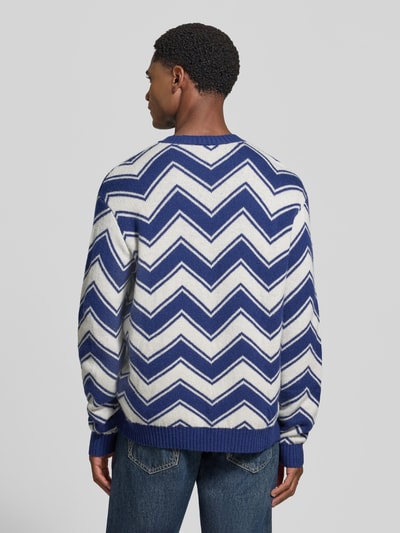 Männermodel trägt Strickpullover aus Schurwolle-Mix mit Rundhalsausschnitt von Armani Exchange mit blau-weißem Zickzackmuster, Regular Fit, gerippte Abschlüsse, Rückenlänge 65 cm, Ärmellänge 69 cm, Ganzkörperansicht Rückansicht.