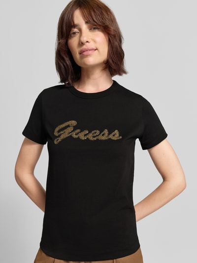 Frauenmodel trägt T-Shirt mit Logo aus Perlen von GUESS in Schwarz, Rundhalsausschnitt, Regular Fit, reine Baumwolle, Nahaufnahme Oberkörper.