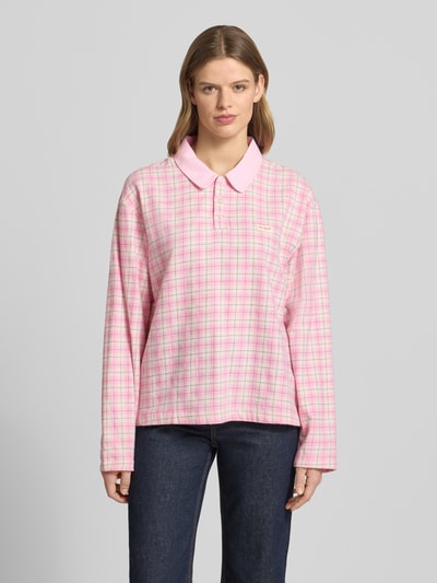 Frauenmodel trägt Oversized Poloshirt mit Label-Detail Modell 'Diana' von OH APRIL aus Reine Baumwolle, rosa kariert, Longsleeve, Knopfleiste, Rückenlänge bei Größe S 66 cm, Ganzkörperansicht von vorne.