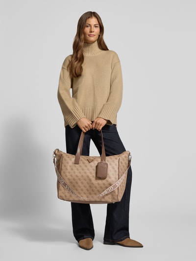 Frauenmodel trägt Handtasche in Leder-Optik Modell 'TAMARA' von GUESS mit Logo-Detail in Beige, Struktur-Optik, Ganzkörperansicht von vorne. Damen Handtasche von GUESS, Hauptfach mit Reißverschluss, schmale Schulterriemen, Breite 52 cm, Länge 38 cm, Tiefe 22 cm, Riemen 100 cm.