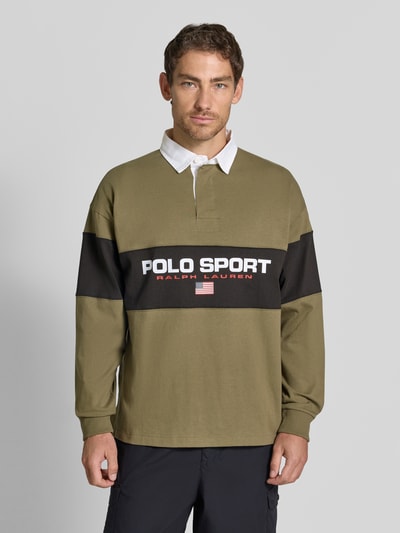 Męski model nosi Relaxed Fit Poloshirt aus reiner Baumwolle von Polo Ralph Lauren, oliwkowa z czarnym i białym, nadruk z logo, tekstura gładka, Ganzkörperansicht von vorne.