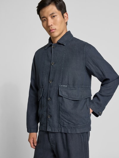 Männermodel trägt Hemdjacke aus reinem Leinen von Closed in Dunkelblau mit Pattentaschen und Knopfleiste, Regular Fit, Nahaufnahme Oberkörper.
