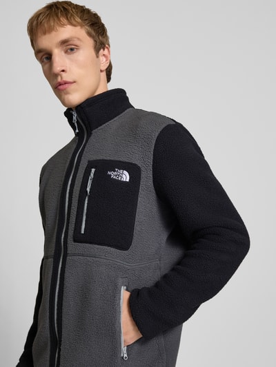 Männermodel trägt Fleecejacke mit Logo-Stitching Modell 'Yumiori' von The North Face in Grau und Schwarz aus Fleece, Nahaufnahme Oberkörper. Gerader-Schnitt, Stehkragen, Reißverschluss, Brusttasche mit Reißverschlusstasche, seitliche Reißverschlusstaschen, Rückenlänge 70 cm, Ärmellänge 68 cm bei Größe M.