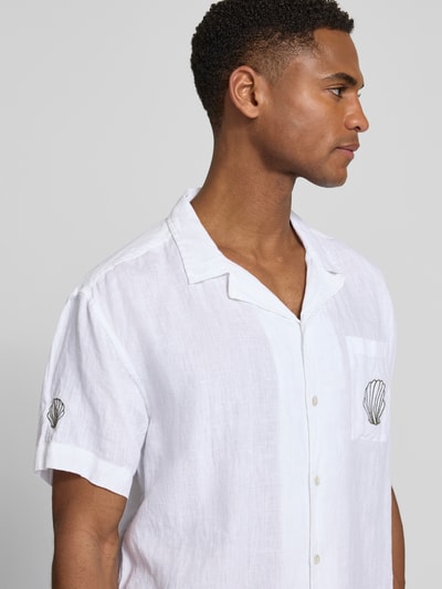Männermodel trägt Regular Fit Leinenhemd mit Stitchings Modell 'Ilfracombe' von BOARDIES in Weiß mit Muschel-Details, Nahaufnahme Oberkörper. Reines Leinen, Reverskragen, Brusttasche, kurze Ärmel, sichtbare Stoffstruktur.