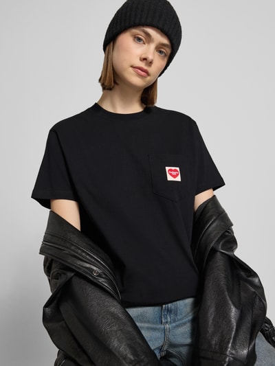 Kobiece modelka nosi damski t-shirt z bawełny z prostym krojem, okrągłym dekoltem, brustaszą i naszywką z logo, długość tyłu 58 cm, T-Shirt mit Label-Patch od Carhartt Work In Progress, zdjęcie całej sylwetki z przodu.