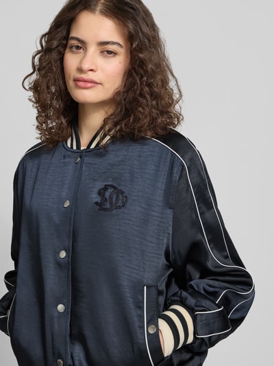 Frauenmodel trägt Bomber Jacke mit Logo-Stitching Modell 'VARSITY' von Superdry in Satin mit Lockerer-Schnitt, Nahaufnahme Oberkörper.