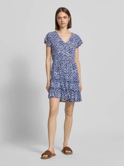 Frauenmodel trägt Tailliertes Freizeitkleid aus reiner Viskose Modell 'CLAUDETTE' von Only mit blau-weißem Allover-Muster, Mini-Länge, V-Ausschnitt, kurzer Knopfleiste, Kurzarm und Volantsaum, Webware-Optik; Ganzkörperansicht von vorne.